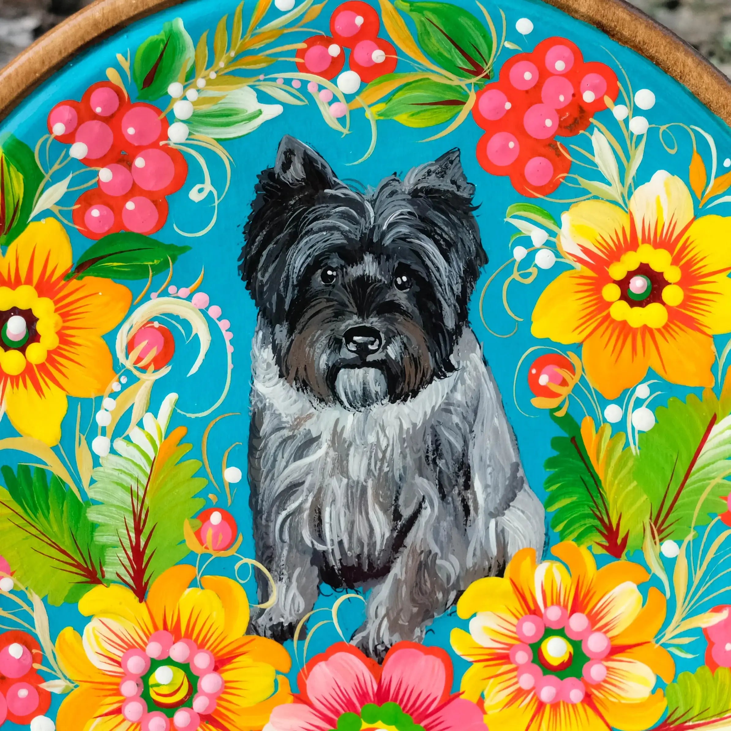 Decorative plate with a black dog illustration surrounded by colorful flowers on a wooden background.