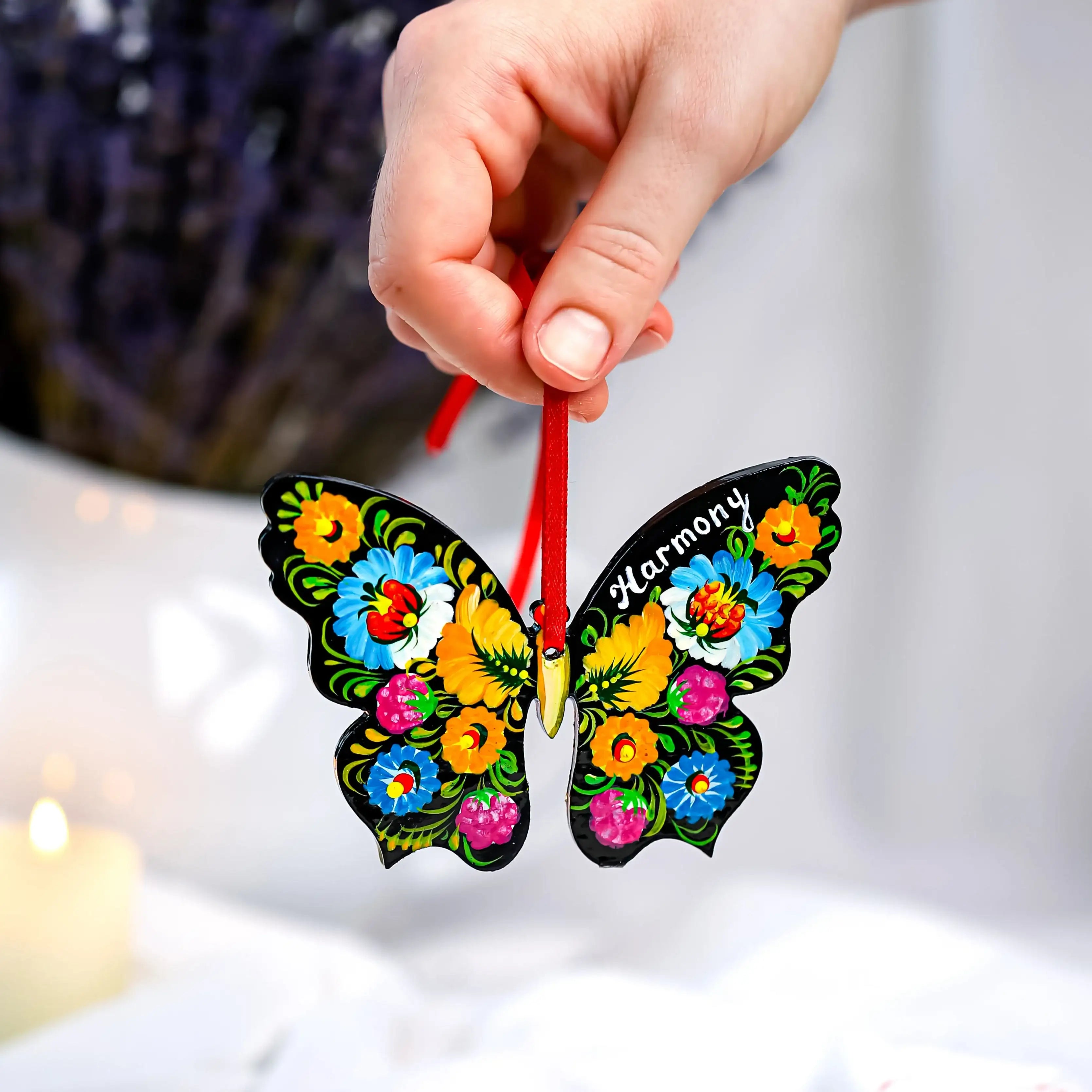 Colorful butterfly-shaped ornament with floral patterns held by a hand against a blurred background.